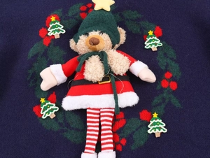 Detail of a 3D teddy bear doll accessory with festive holiday scarf on a navy blue knit sweater