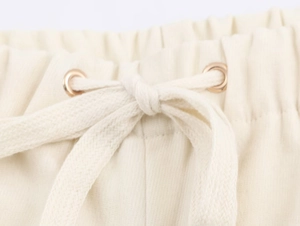 Dettaglio dell'elastico in vita beige con coulisse piatta e occhielli in metallo sui pantaloni