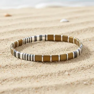 Detail of bohemian Tila bead stretch bracelet with gold and silver enamel beads on sand