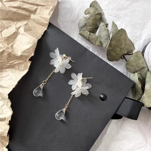 Detail of floral earrings with white matte petals, gold chains and teardrop pendants