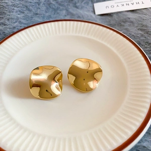 Close-up of gold irregular round stud earrings with wavy metallic texture on a white plate