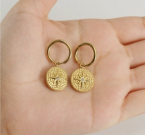 Détail de boucles d'oreilles créoles dorées 18K avec pendentif disque étoile et diamant