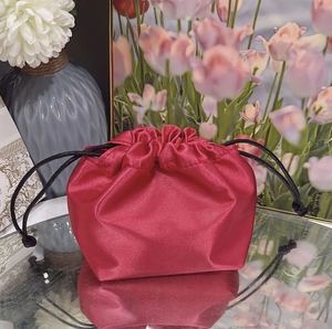 Close-up of a red satin drawstring jewelry pouch with silk texture and black cords