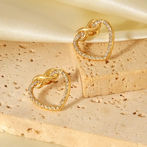 Golden heart-shaped stud earrings with sparkling zircon stones on a beige stone surface