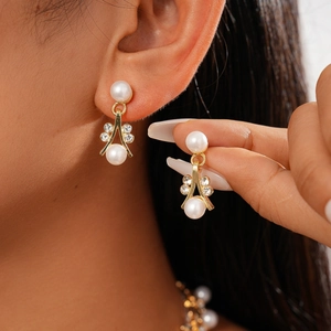 Elegant gold drop earrings with white pearls and sparkling floral rhinestones on model