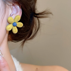 Detail of velvet flower earring in yellow and blue worn by a female model