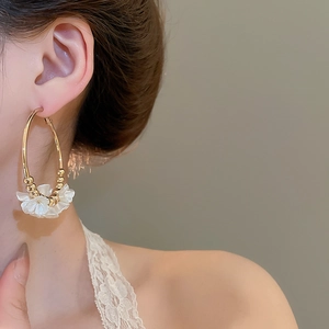 Close-up of golden hoop earrings with elegant white acrylic flower petals on a model