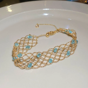 Detail of gold beaded mesh bracelet with light blue crystals on a white ceramic plate