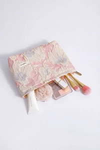 Macro shot of floral embossed makeup bag with brushes and cosmetics on white background