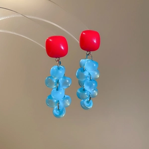 Macro view of square red resin earrings with blue grape tassel pendants and silver needles