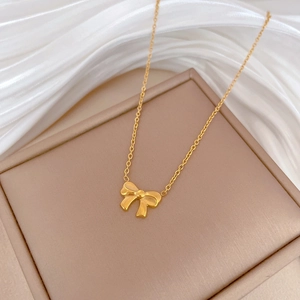 Minimalist gold bow necklace displayed on a beige jewelry box with white silk background