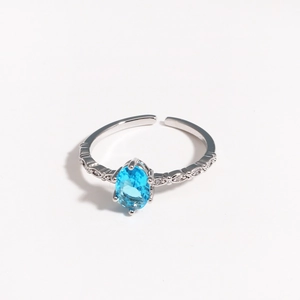 Macro detail of silver open ring with oval blue zircon and pavé diamond band accents
