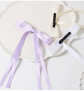 Detailed view of satin bow hair clips in purple and white on a ceramic plate