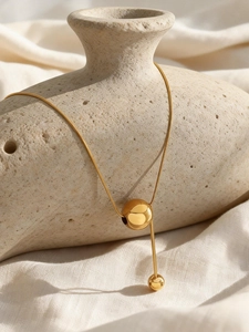 Détail macro du collier pendentif boule et gland en acier inoxydable doré sur un vase