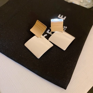 Macro detail of geometric brushed metal square earrings with gold and silver finish