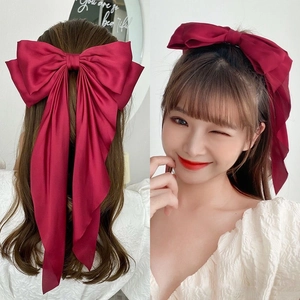 Close-up of elegant red satin oversized bow hair clip with long ribbons worn by a model