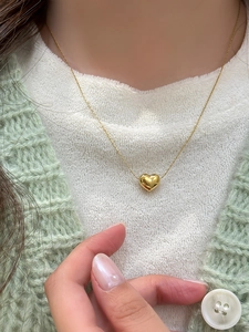 Polished gold heart pendant necklace shown on neck with soft knit cardigan background
