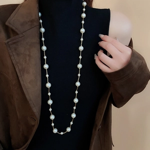Detail of elegant long faux pearl necklace layered over a black turtleneck sweater