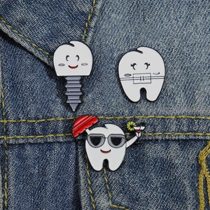 Detailed view of three cute cartoon tooth enamel pins on dark blue denim fabric background