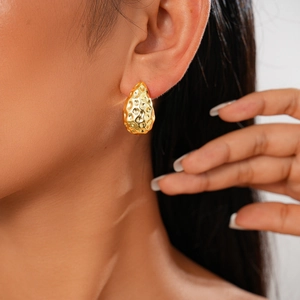 Détail de boucles d'oreilles gouttes dorées à surface texturée portées par un mannequin