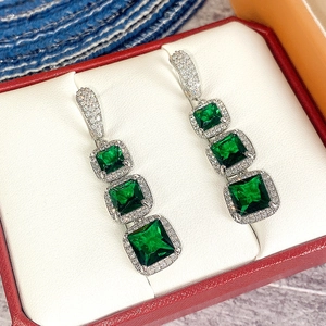 Macro view of tiered silver earrings with square emerald-cut green zircons and white halos