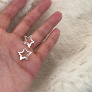 Close-up of silver hollow star-shaped huggie earrings held by hand on white fur background