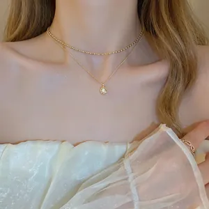 Detail of layered gold double chain necklace with pearl pendant on model neck