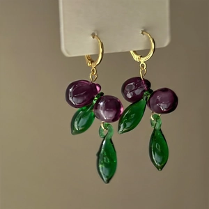 Close-up detail of gold-plated grape earrings with purple glass beads and green leaves
