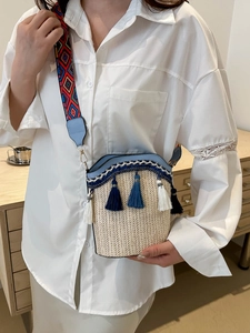 Detail of woven straw bucket bag with blue leather trim and colorful geometric strap