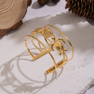 Dettaglio di un bracciale rigido multistrato in acciaio dorato con ciondoli a tartaruga