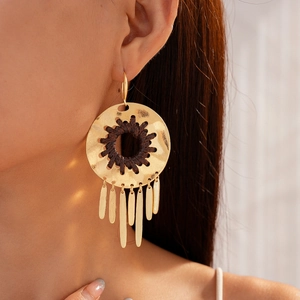 Gros plan de boucles d'oreilles bohèmes dorées avec texture tissée et pompons en métal