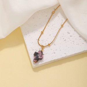 Detailed view of cross pendant made of pink and black natural stone on gold bead chain