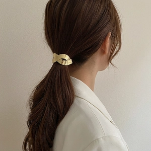 Elegant gold twisted metal hair clip with polished finish shown on a low ponytail hair style