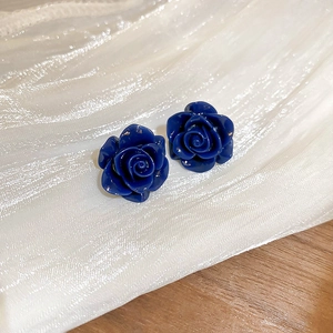 Vue macro de boucles d'oreilles rose bleu foncé sur tissu blanc et fond grain de bois