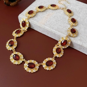 Detailed view of vintage gold necklace with oval red gemstones and white floral accents
