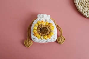 Detail of hand-knitted sunflower drawstring pouch with heart pendants on pink background
