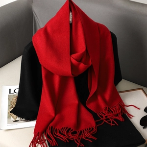 Soft red cashmere-feel scarf with fringe hanging in a cozy home setting for winter