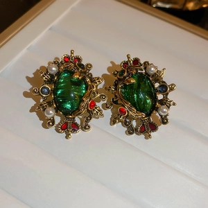 Close-up of vintage emerald green earrings with pearls and crown detail on white tray