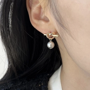 Detail showing a golden knot stud earring with a hanging pearl on a female model