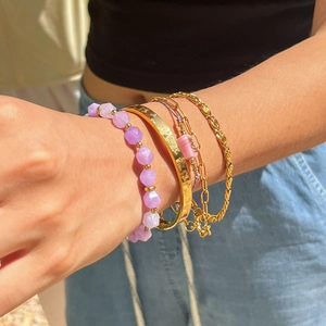 Close-up of stacked gold-plated bracelets with amethyst beads and a butterfly bangle