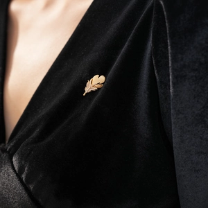 Macro detail of a golden feather brooch with zircons pinned on black velvet fabric