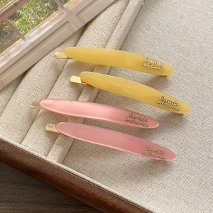 Close-up of four elegant acetate hair barrettes in cream yellow and soft cherry blossom pink