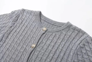 Close-up of grey cable-knit cardigan featuring round metal buttons and fine fabric texture