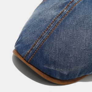 Detail of washed denim flat cap showing orange double-stitching and brown leather brim edge