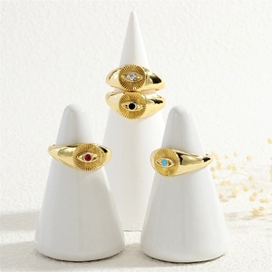 Detail of four gold evil eye rings with multi-colored zircon stones on white display stands