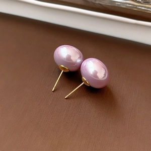 Macro detail of glossy purple pearl earring with a gold pin on dark background