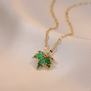 Titanium steel necklace featuring a golden maple leaf pendant with green zircons on silk