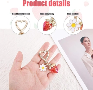 Detail view of heart buckle, resin strawberry, and alloy daisy pendant on a keychain