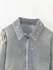 Detail of distressed denim jacket featuring heavy frayed holes and metallic zipper