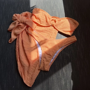 Detailed flat lay of orange textured fabric three-piece bikini set with buckle and sarong